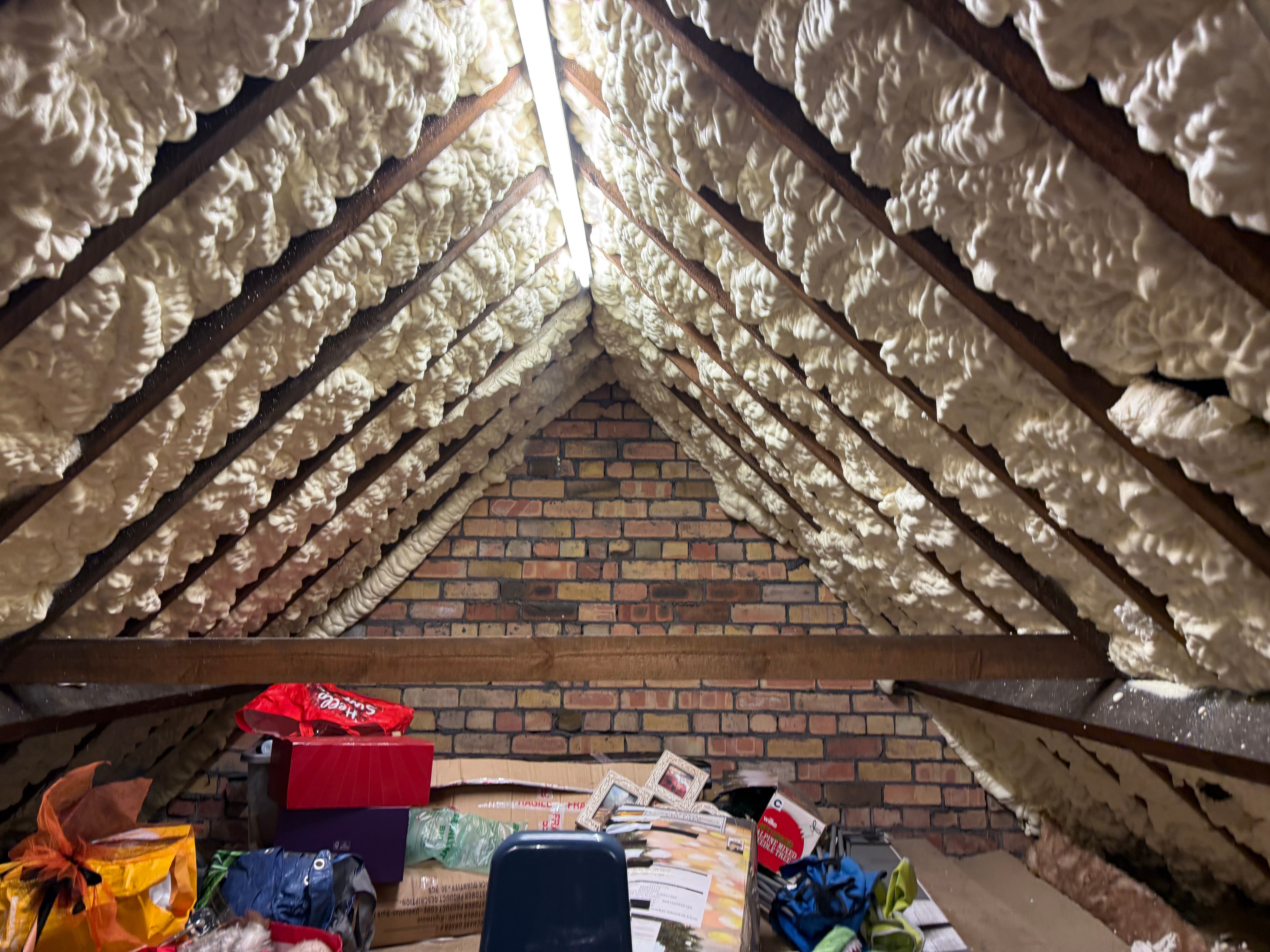 Open-cell spray foam applied across roof rafters in a residential loft — pale, spongy and textured